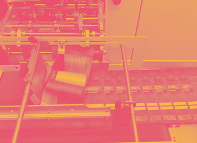 Foto: Flyer werden in der Produktionsmaschine gedruckt. Darüber liegt ein Farbfilter in Gelb und Pink.